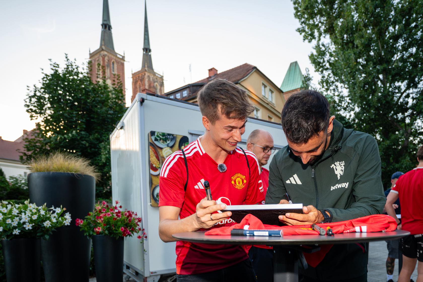 Bruno Fernandes signs shirt with cathedral in background in Wroclaw, Poland