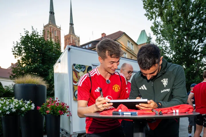 Bruno Fernandes signs shirt with cathedral in background in Wroclaw, Poland